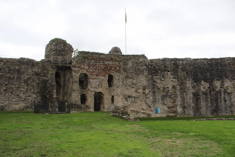 Inner ward of Denbigh Castle with ruined buildings against the curtain wall and the Welsh flag above, October 2026