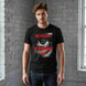 Man wearing a black t-shirt with 'Big Brother is Watching You' design against a brick wall.