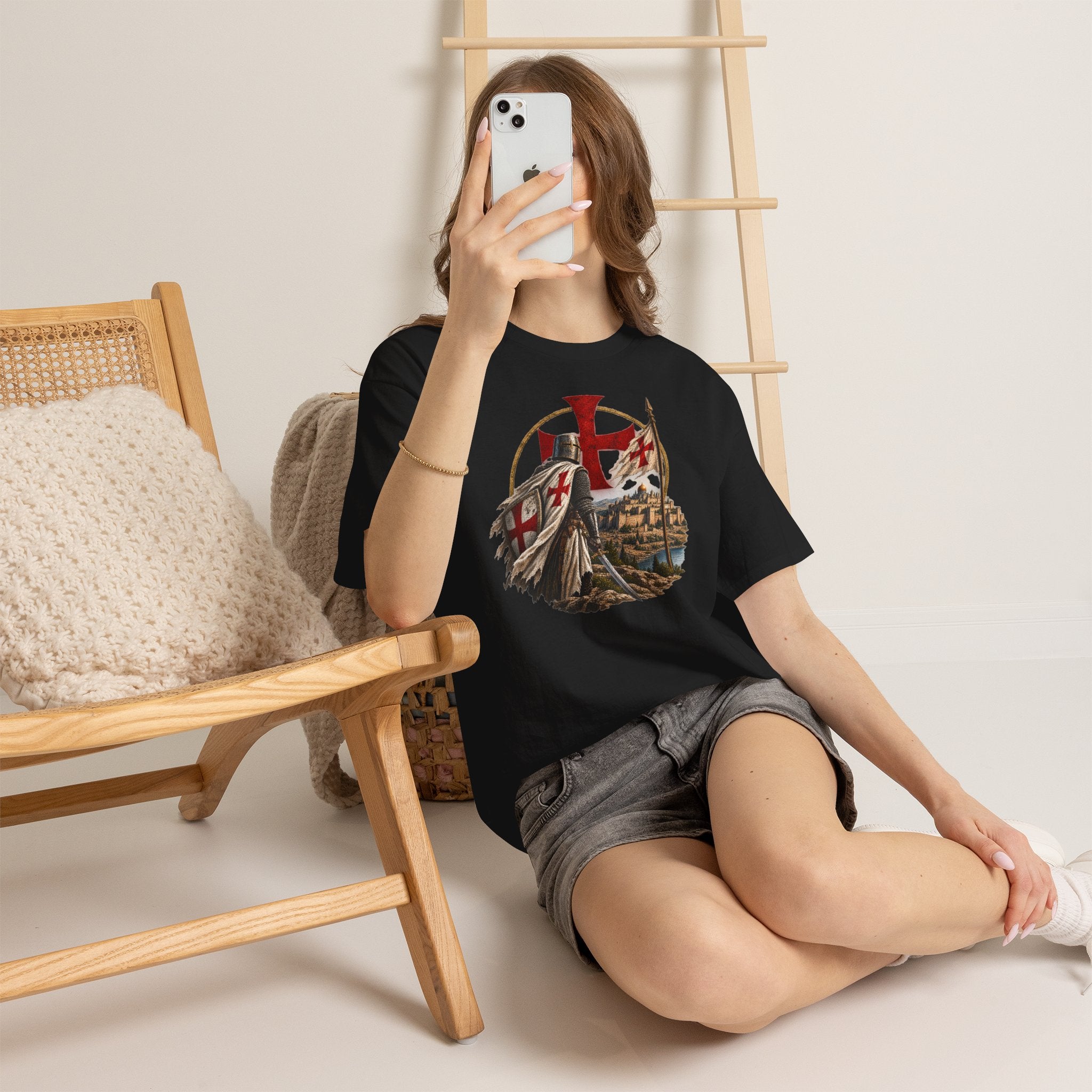 Person wearing a black t-shirt with a graphic design, sitting on the floor with a wooden chair and ladder in the background.