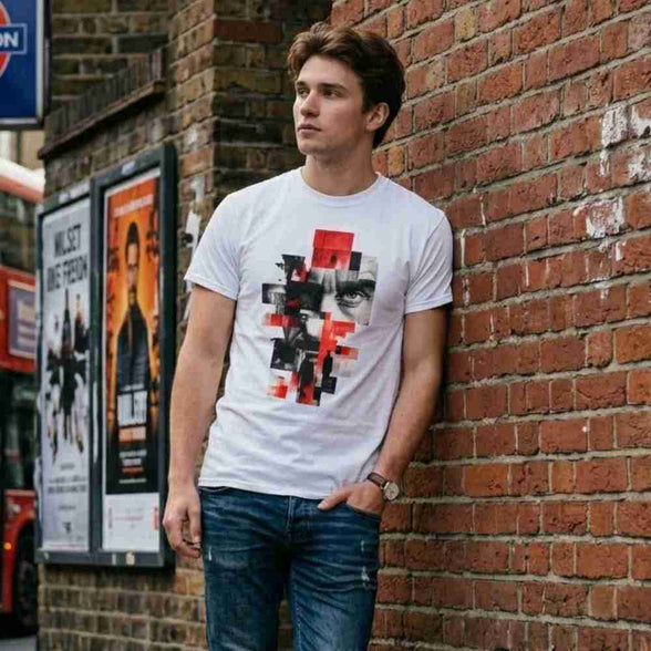 Man wearing a graphic t-shirt leaning against a brick wall with posters on a bus stop.