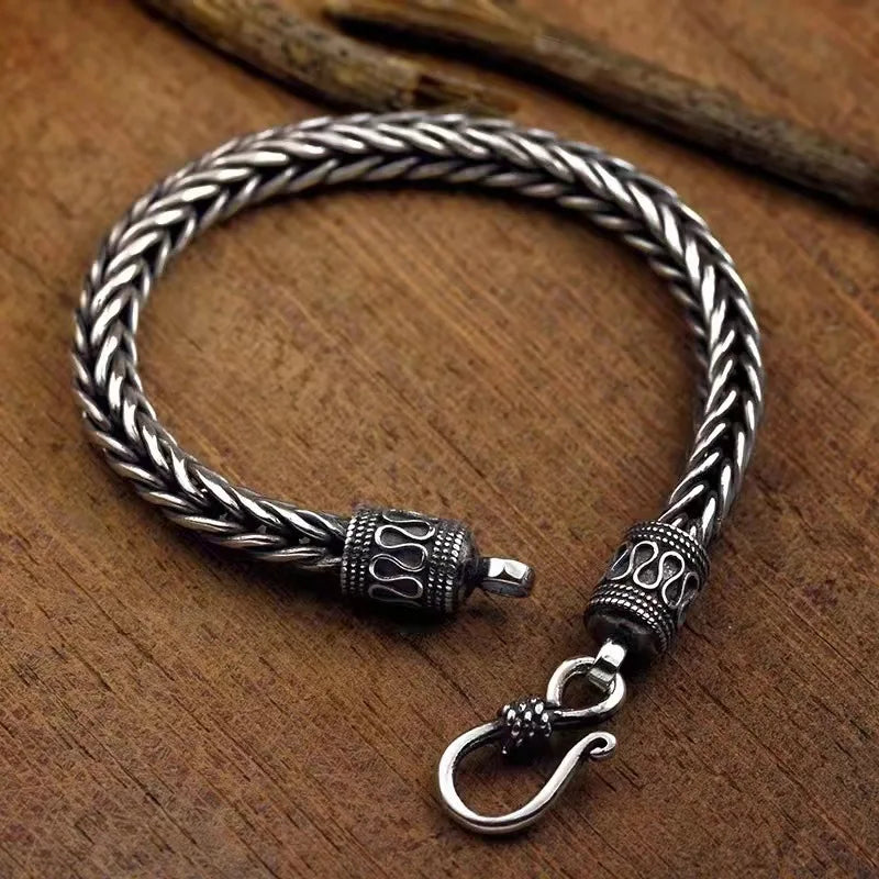 Silver braided bracelet with intricate designs on a wooden surface