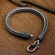 Silver braided bracelet with intricate designs on a wooden surface