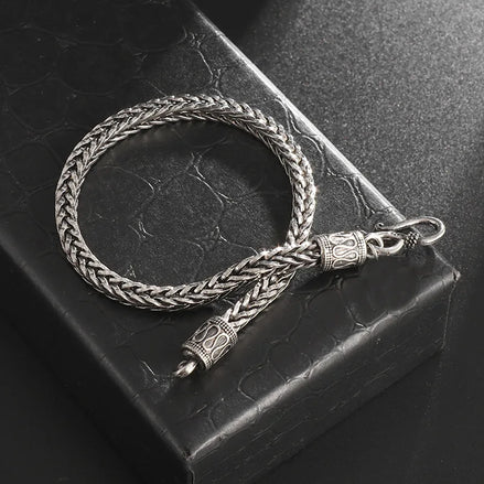 Silver braided bracelet with intricate designs on a textured black surface
