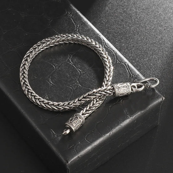 Silver braided bracelet with intricate designs on a textured black surface