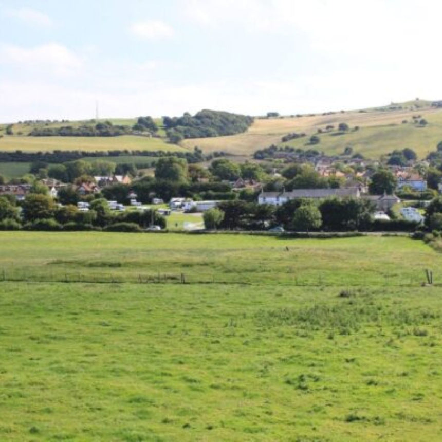 Green field with a village in the background under a blue sky.