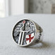 Silver ring with a detailed design featuring a knight, sword, and shield on a light fabric background.