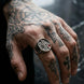 Hand with tattoos wearing a ring against a blurred background