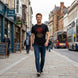 A man walking down a city street wearing a black t-shirt with a red dragon graphic and the text 'THE RED DRAGON RISES'.