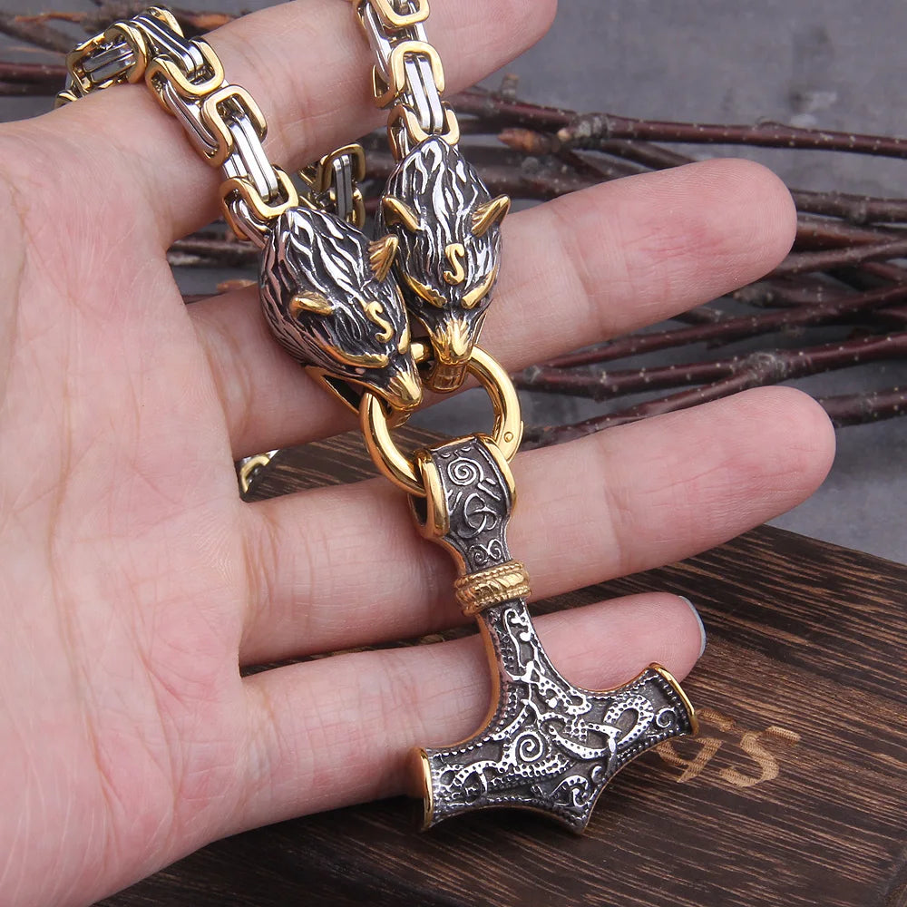 Hand holding a decorative hammer pendant with intricate designs on a wooden surface.