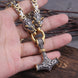 Hand holding a decorative hammer pendant with intricate designs on a wooden surface.