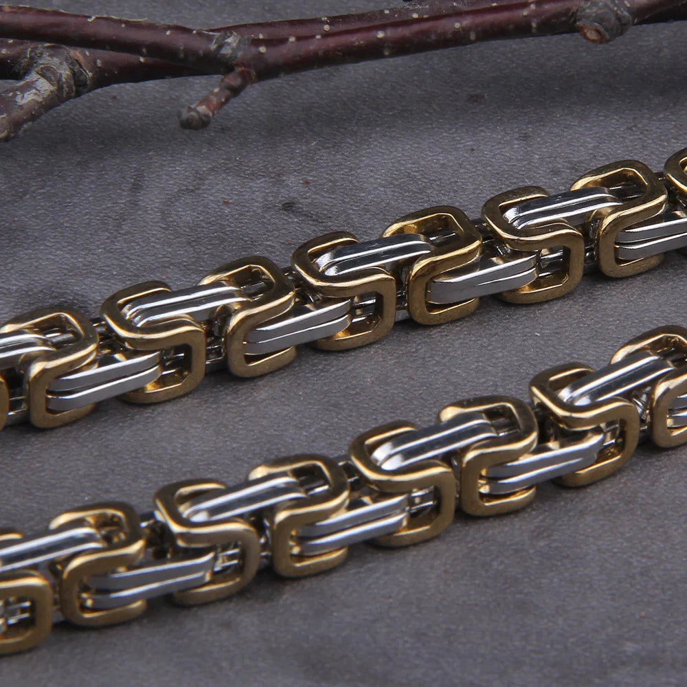 Gold and silver chain bracelet on a dark surface with branches in the background