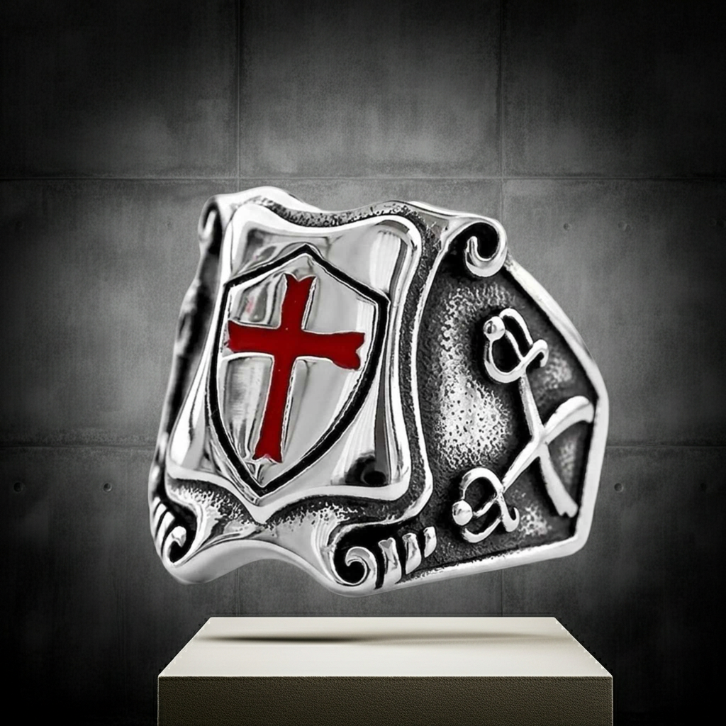 A silver-toned ring featuring a shield with a red cross and crossed keys, displayed on a pedestal against a dark gray background.