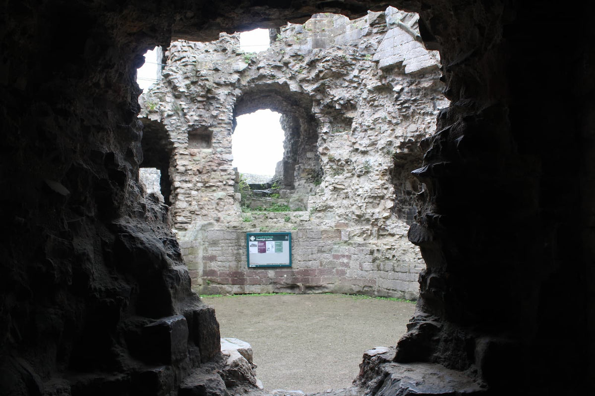 View out of a dark chamber in the great gatehouse of Denbigh Castle towards an information board, October 2026