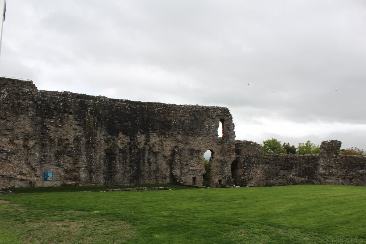 Ruined curtain wall around the grassy inner ward of Denbigh Castle, with an arched opening in the wall, October 2026