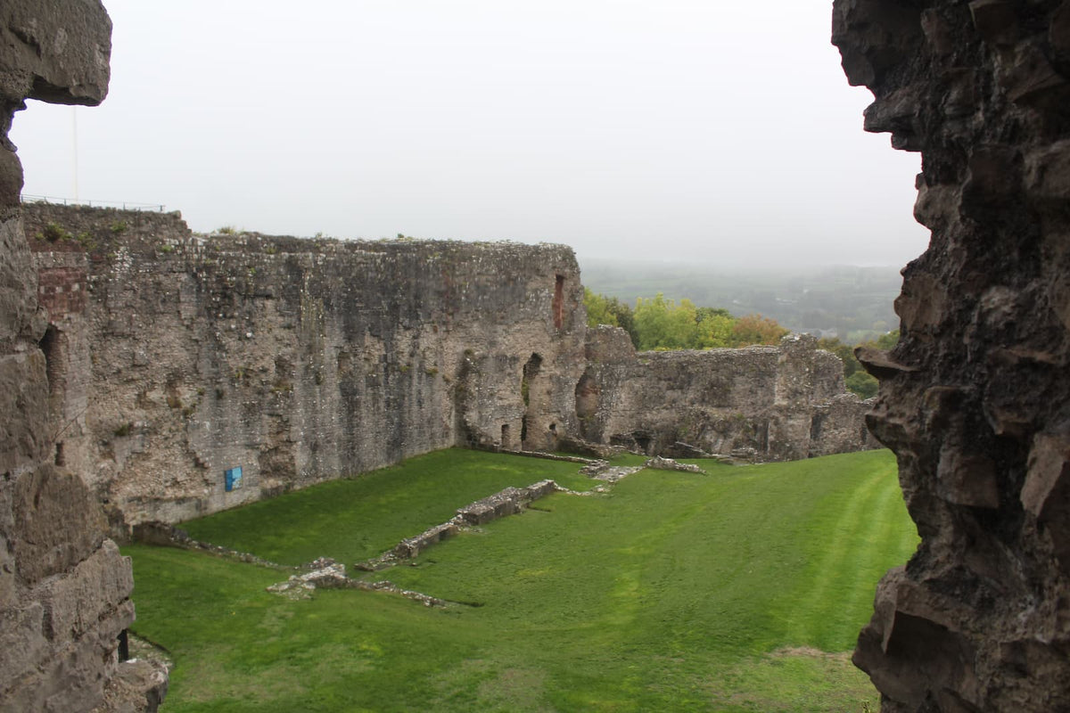 View through a gap in a ruined wall across the inner ward of Denbigh Castle to the hills beyond, October 2026