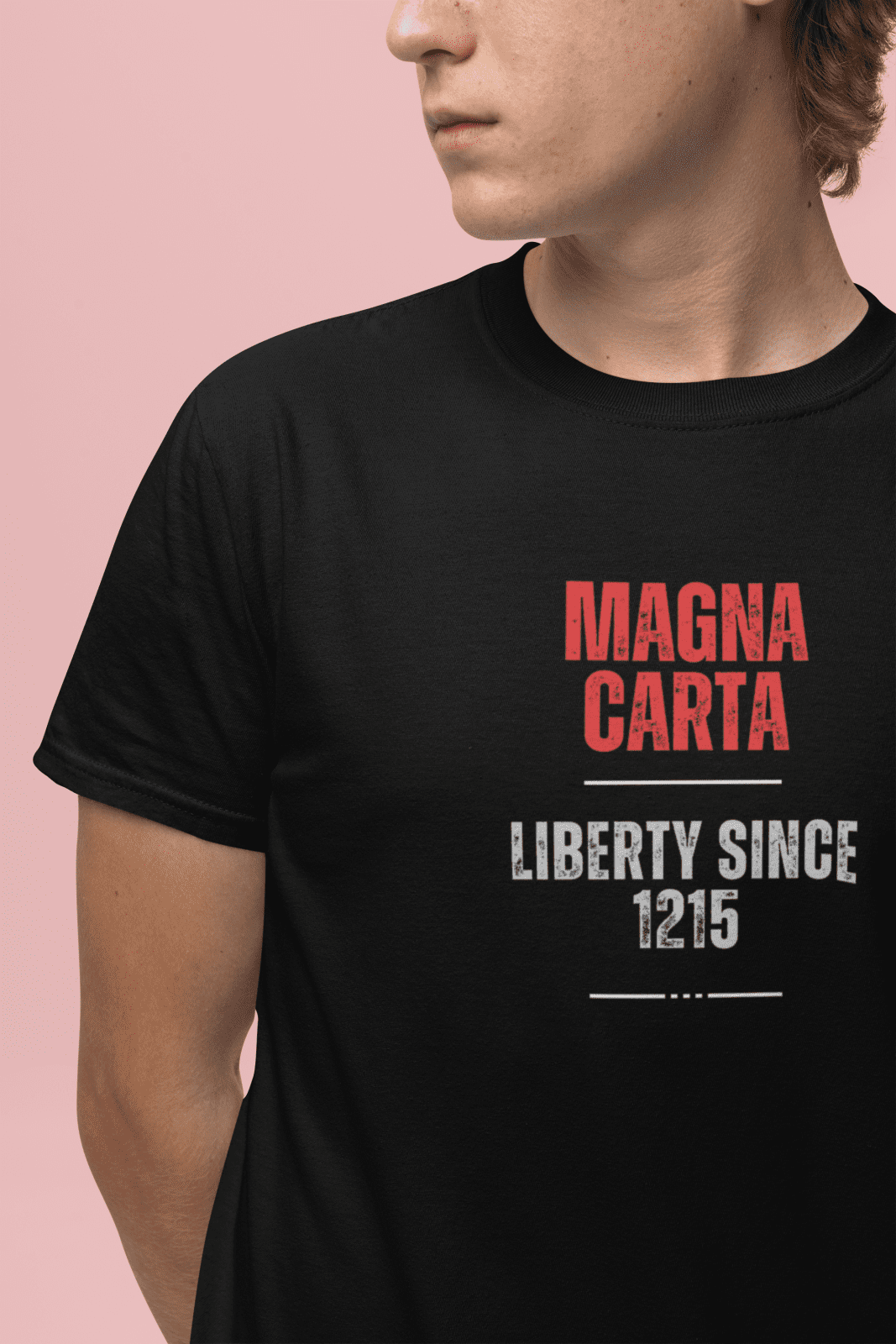 Wearing the Magna Carta T-Shirt: Liberty Since 1215, a person stands against a pink background, looking to the side.