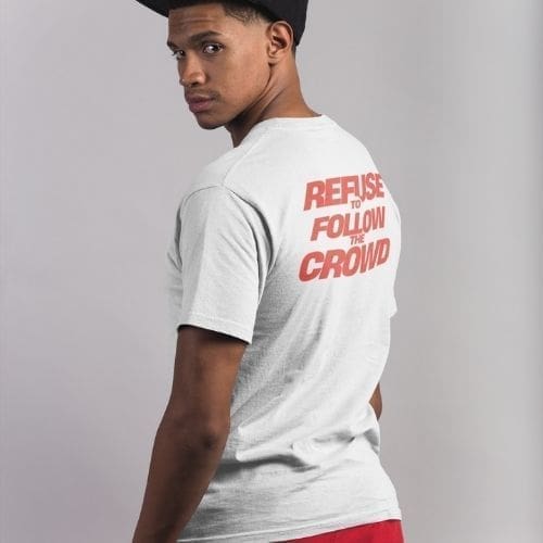 A man in a backwards black cap and a Refuse to Follow the Crowd T-Shirt, featuring bold red lettering on the back, glances over his shoulder against a plain background.