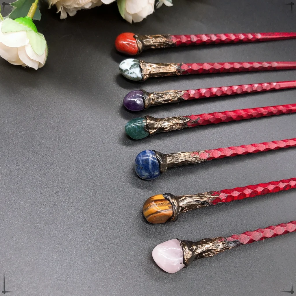 Seven 19CM natural crystal stone magic wands—featuring amethyst, tiger eye, labradorite, and red agate—are lined up on a dark surface; white flowers peek in at the corner. Perfect for home decor or witchcraft gifts.