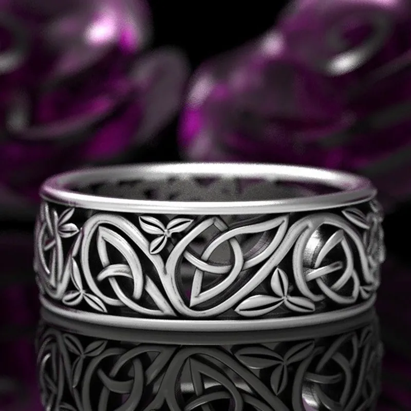 The Viking Wolf Knot Ring features intricate Celtic knot and leaf designs in silver, displayed on a reflective black surface with blurred purple shapes in the background.