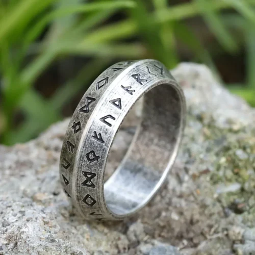 The Viking Letter Ring | Norse Initial Runes Jewellery, engraved with runic symbols, rests on a rough stone surface with blurred green plants in the background.