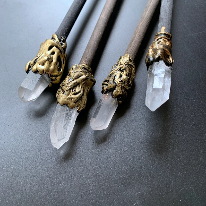 The Quartz Point Crystal Wand – Medieval Magic and Mindfulness is displayed on a dark surface, its gold wire and ornate gemstone decorations highlighted by colorful crystals and stones.