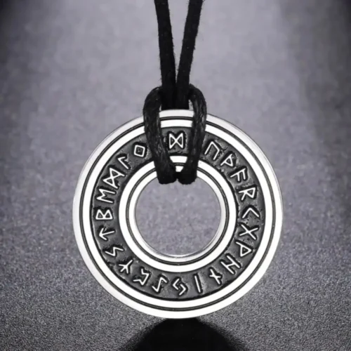 The Norse Runes Viking Pendant Amulet, a round metallic piece engraved with runes, hangs on a black cord and is shown against a dark, textured background.
