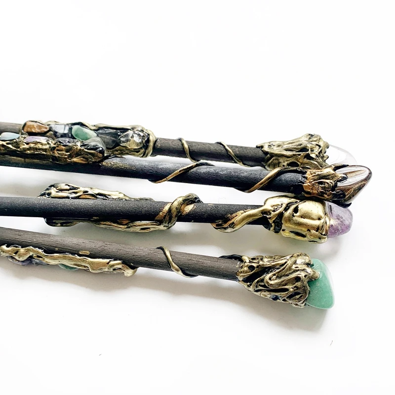 The Quartz Point Crystal Wand – Medieval Magic and Mindfulness is displayed on a dark surface, its gold wire and ornate gemstone decorations highlighted by colorful crystals and stones.