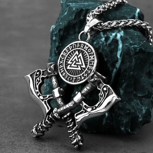 The Double Axe Viking Necklace features two crossed axes and a Viking medallion with runes and a Valknut symbol, showcased on a teal stone background.